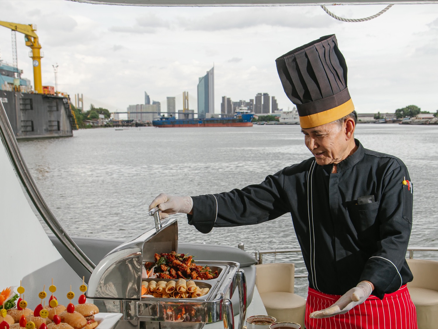 Chef Pradit Namo plating dishes at the buffet, the Chao Phraya behind him