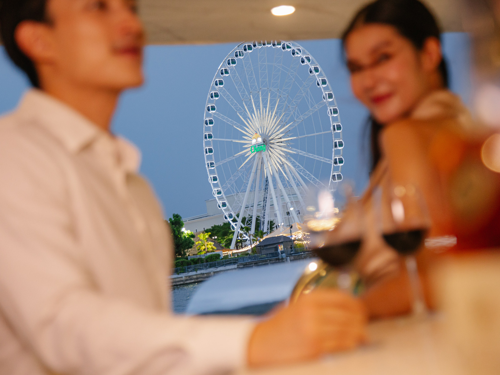 Elegantly dressed guests on deck with Bangkok landmarks along the Chao Phraya by day